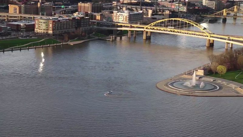 Aerial view of a city with a river, a yellow bridge, and a fountain.