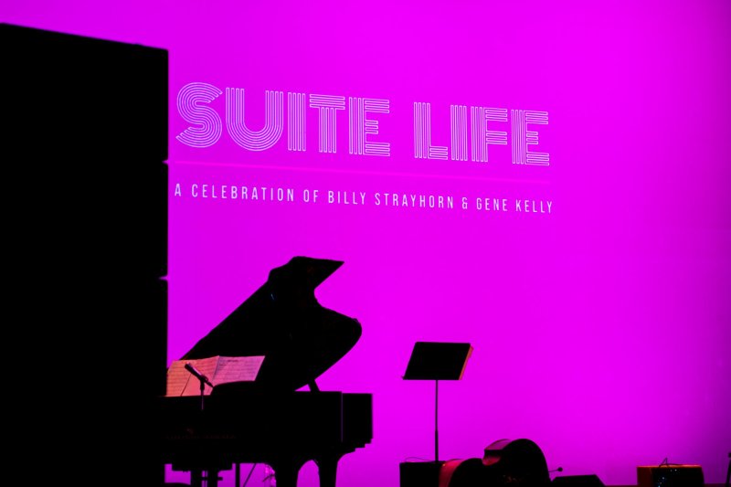 Suite Life" title in white on a bright magenta screen, with a grand piano and music stand silhouetted below.