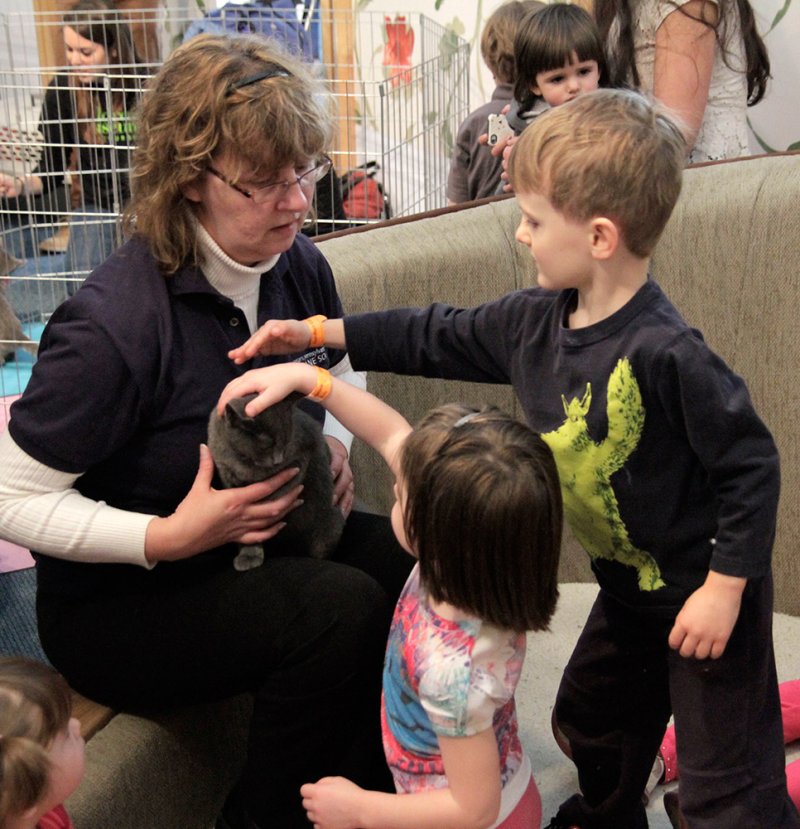 A woman holding a dark gray cat while two young children reach out to pet it.