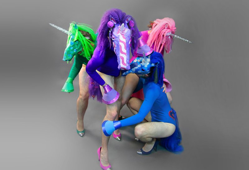 Three people in brightly colored unicorn costumes with human legs, against a gray background.