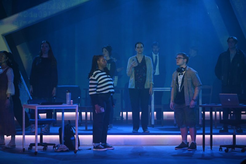 Stage performance of "Dear Evan Hansen" with nine actors under blue light, two central, others in background.