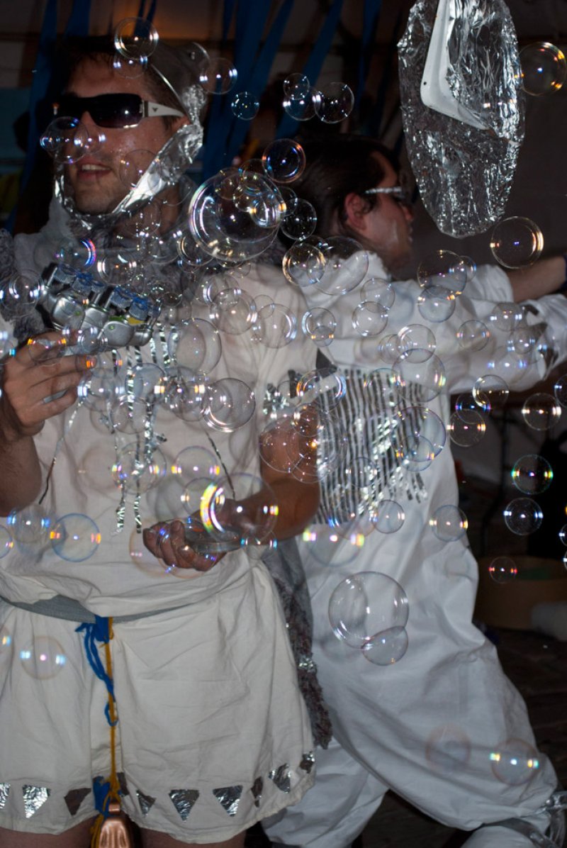 Two people in white outfits and sunglasses surrounded by bubbles.